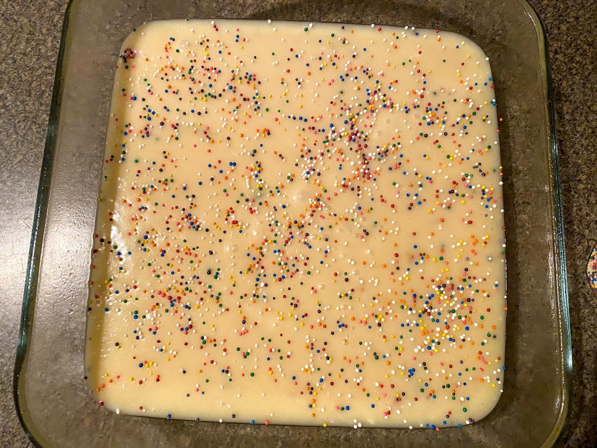 sugar cookie fudge batter with sprinkles on top in a glass pan