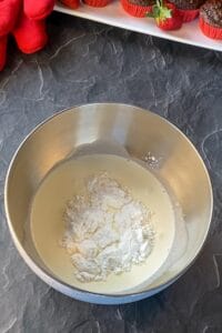 mixing bowl with whipping cream and powdered sugar on a black marble surface