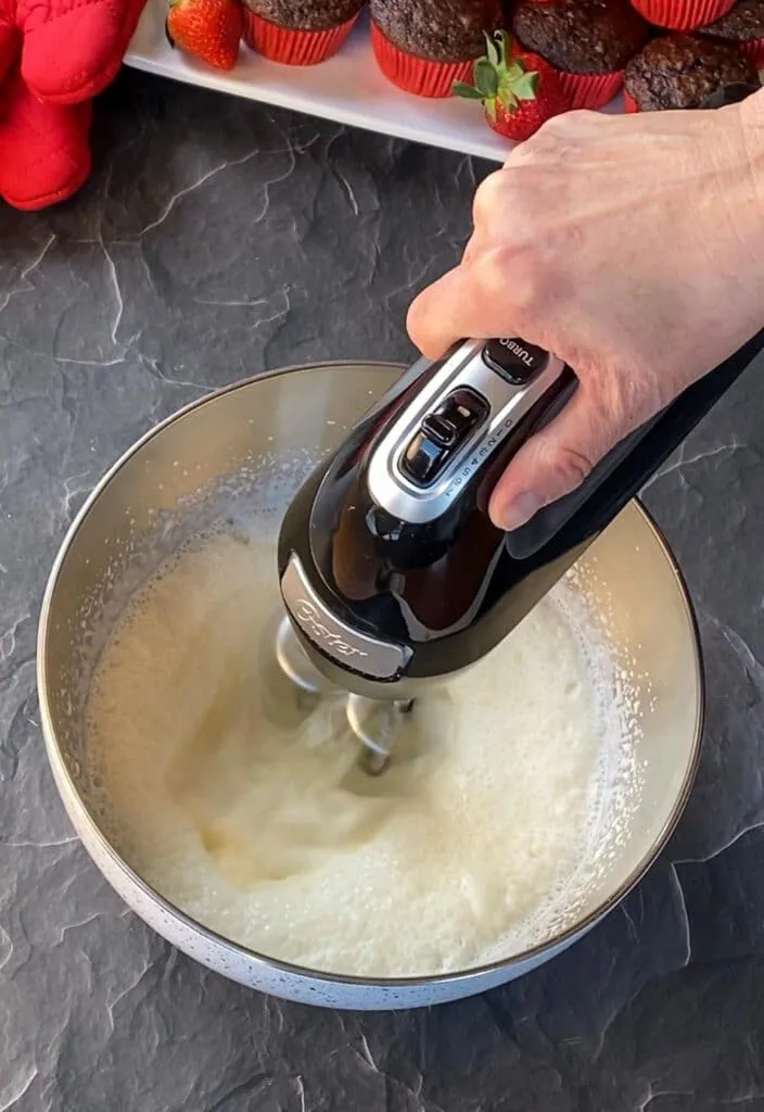 whipping cream and powdered sugar in a mixing bowl, being whipped with electric hand mixer