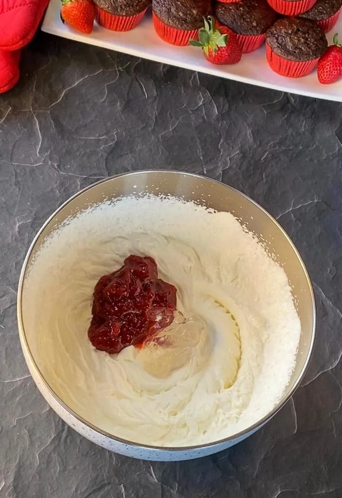jam, vanilla extract and piping gel added to whipped cream powdered sugar mixture in bowl