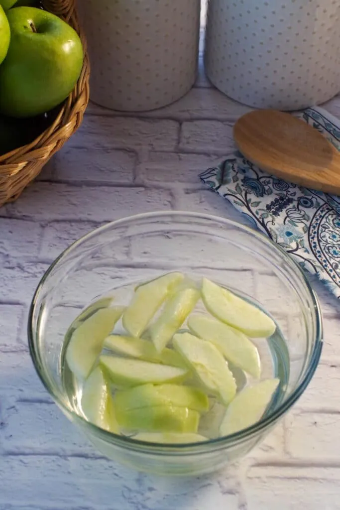 sliced apples in a glass bowl with lemon and water on white surface