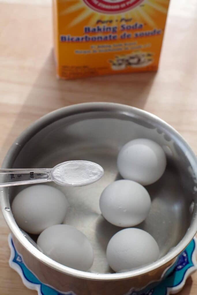 teaspoon with baking soda being held over a pot of eggs ready to be boiled