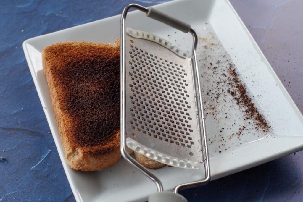 burnt toast being scraped with a microplane grater over a white plate