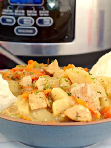 crockpot chicken stew in a blue bowl with biscuits on the side and a slow cooker in the background