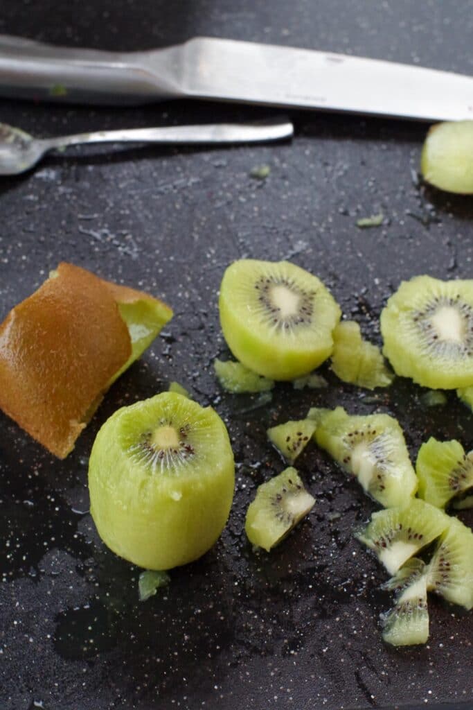 peeled kiwi on a black cutting board