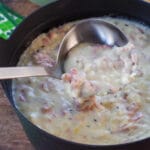 Reuben chowder in a black pot with ladle and clover leaf green and white napkins in the background