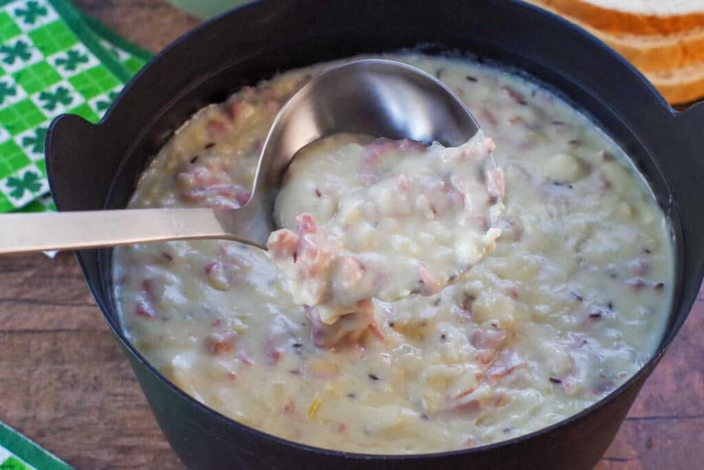 Reuben chowder in a black pot with ladle and clover leaf green and white napkins in the background