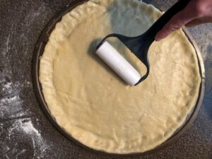 cookie dough pizza crust being rolled out onto pizza pan