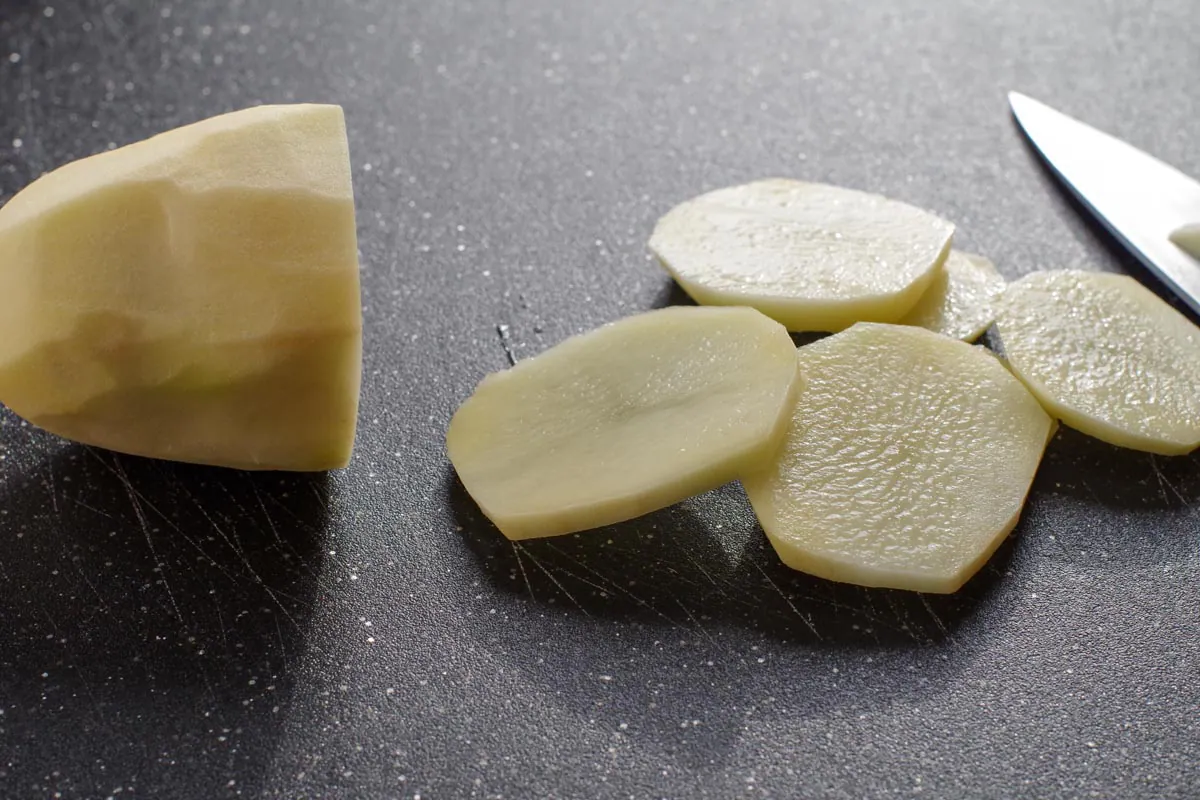 potatoes cut into ⅛ inch slices on black cutting board