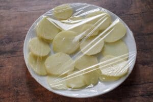 potato slices on white plate covered in plastic wrap