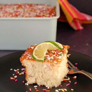 coconut tres leches cake on a black plate with a fork, with a whole cake in the background