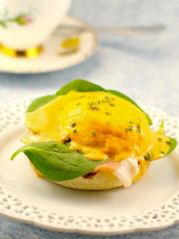 Eggs Benedict with Artichoke Hollandaise on a white plate with lattice edges (and tea cup in the background)