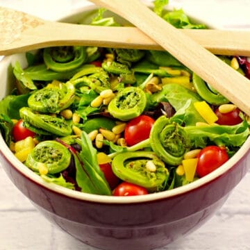 fiddlehead salad in a wine colored ceramic bowl with wooden salad utensils on top