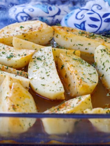 Greek potatoes in a glass pan with a blue patterned oven mitt in the background