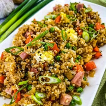 ham fried rice on a white platter with green onions in the background