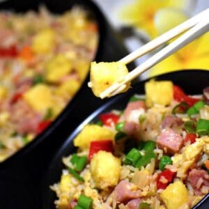 Hawaiian pineapple fried rice in a black bowl with some being lifted out with chopsticks