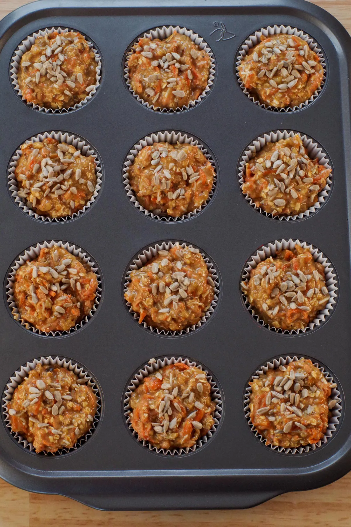 batter in lined muffin tin with sunflower seeds sprinkled on