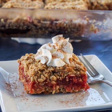 rhubarb square on a white plate, with glass dish of more rhubarb squares in the background