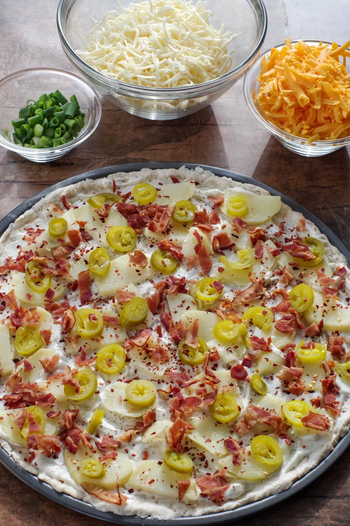 cactus cut potatoes, jalapenos, and bacon on top of sour cream covered pizza dough chili flakes,