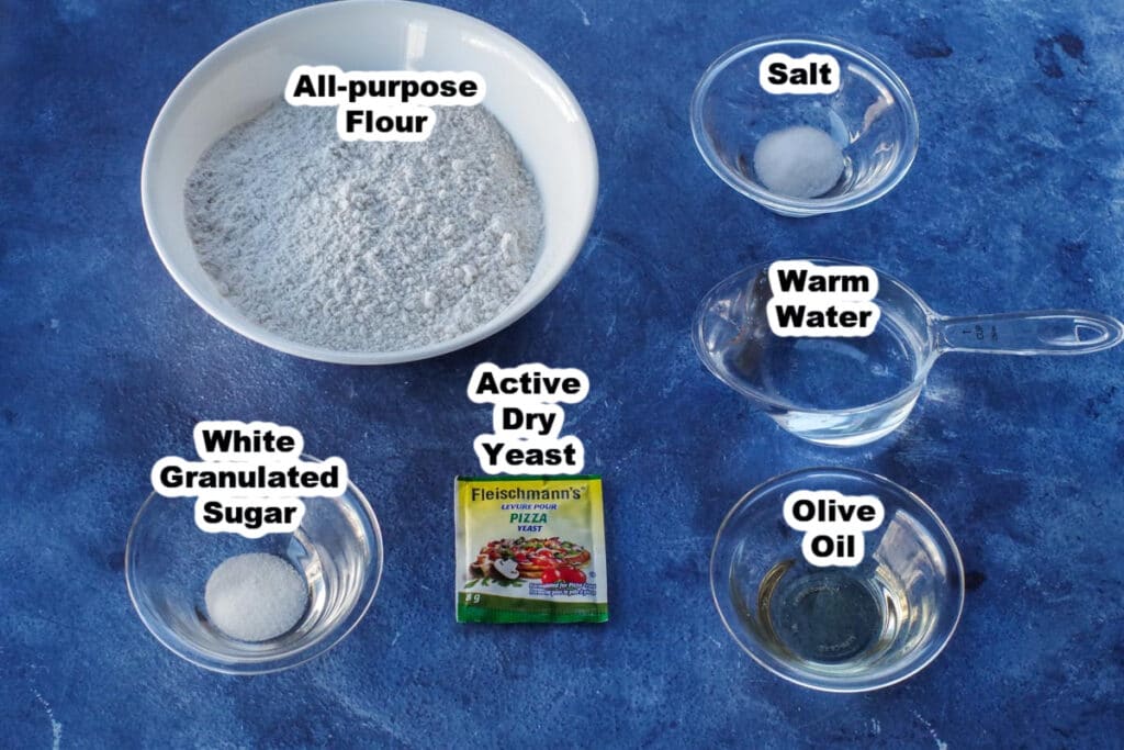labelled ingredients for pizza dough (sugar, salt, water, olive oil, flour and yeast)