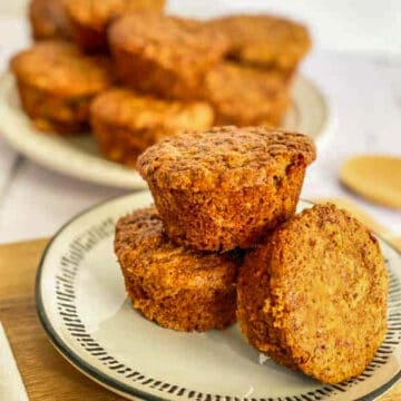 3 bran muffins on a beige plate with trim, with muffins in the background
