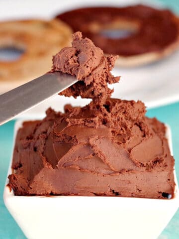 knife with chocolate cream cheese on it, over a white bowl with chocolate cream cheese