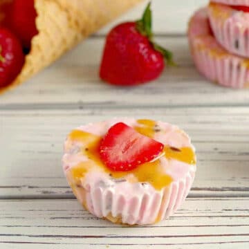 strawberry frozen yogurt cups on a wooden surface with strawberries and cones in the background
