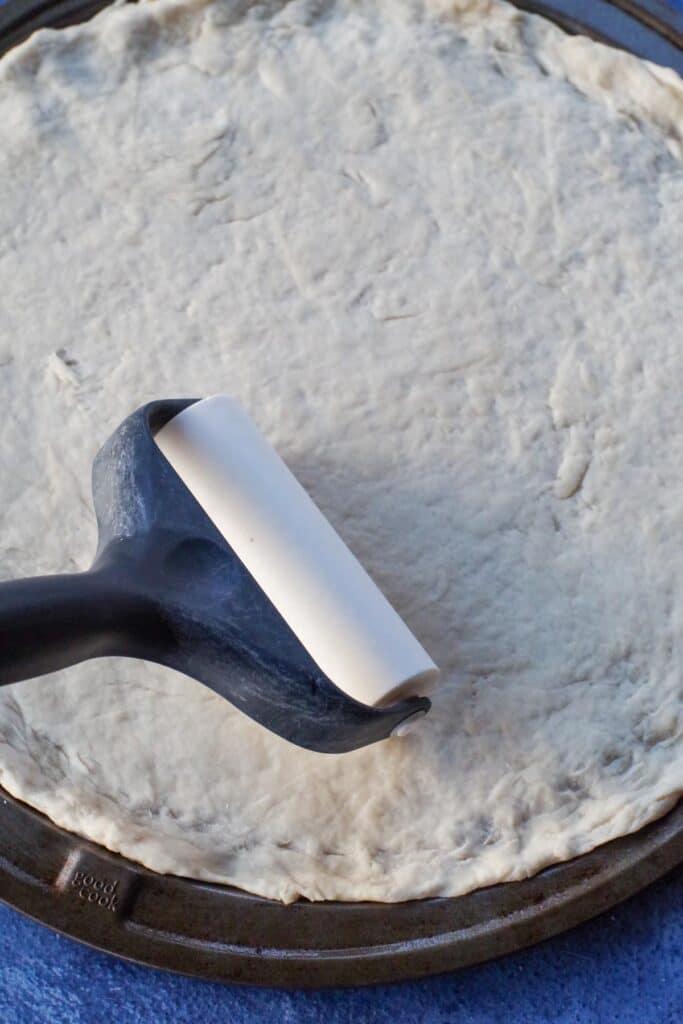 pizza dough being rolled out onto a pan (with a roller) on top of dough