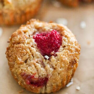 Whole-Wheat-Raspberry-Apple-Bran-Muffin on parchment paper withmore muffins in the background