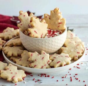 maple shaped cookies with cream cheese dip in a white bowl, with red sprinkles all around