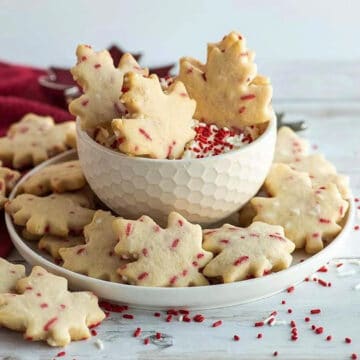 maple shaped cookies with cream cheese dip in a white bowl, with red sprinkles all around