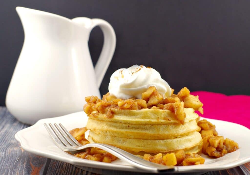 waffles with apple topping on a white plate with white syrup container in background