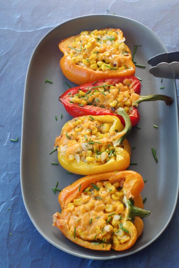 4 stuffed grilled peppers on a long grey platter with thongs leaning on platter