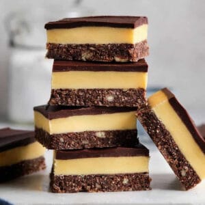 5 Nanaimo bars piled up on a white plate, with one on each side
