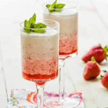 2 strawberry fool parfaits in tall parfait glasses with whole strawberries in the background