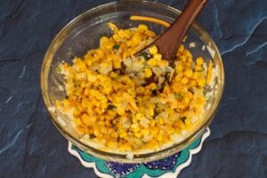 corn, herbs, and cheese mixed into onion mixture in glass bowl