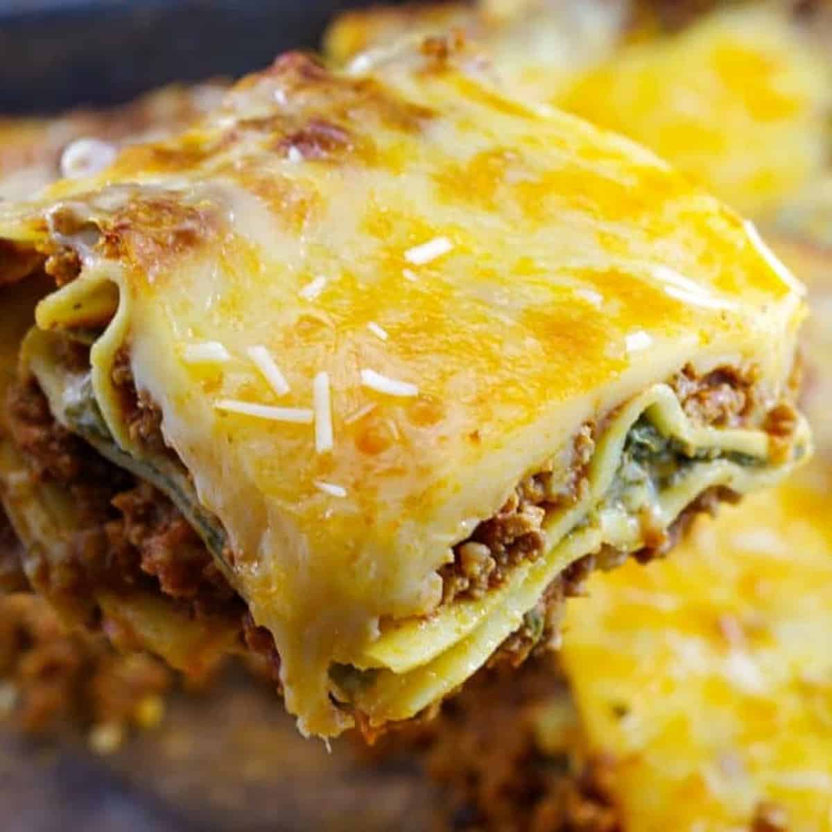 piece of lasagna being held up over container of lasagna