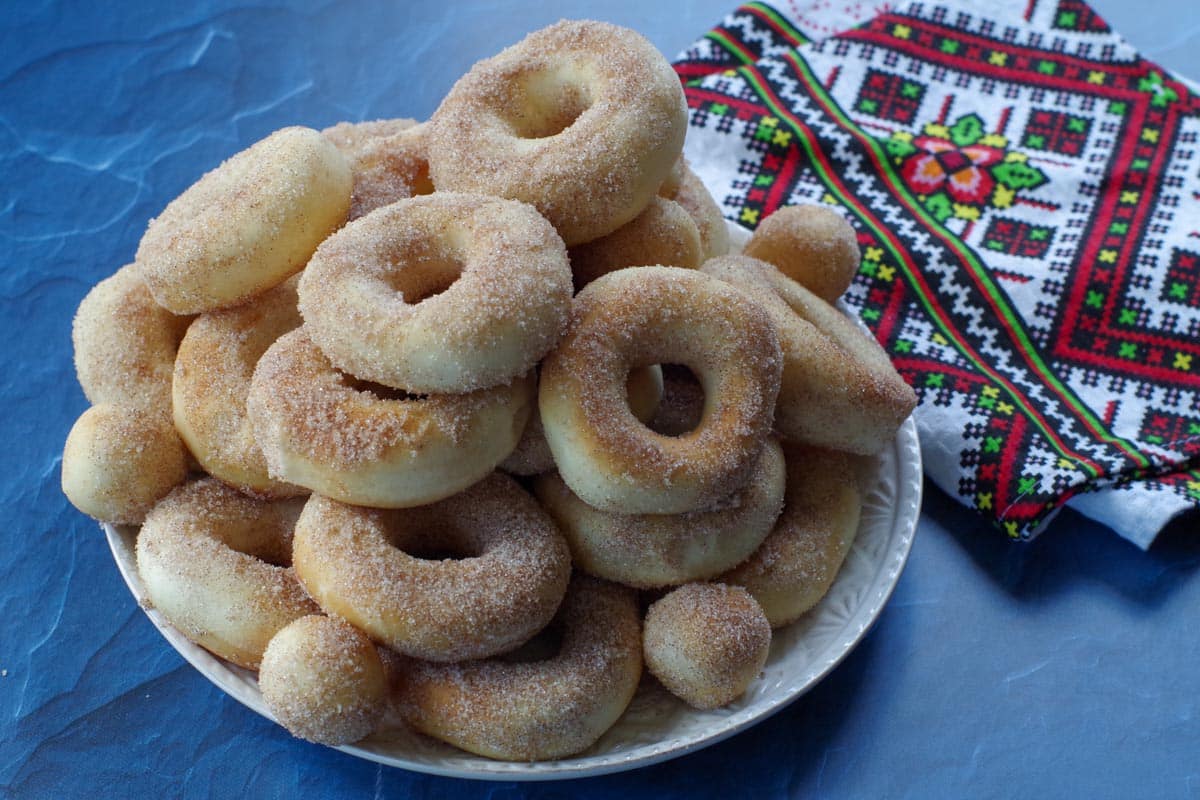 Pampushky Ukrainian donuts on a white plate on blue surface, with Ukrainian print towel on the side
