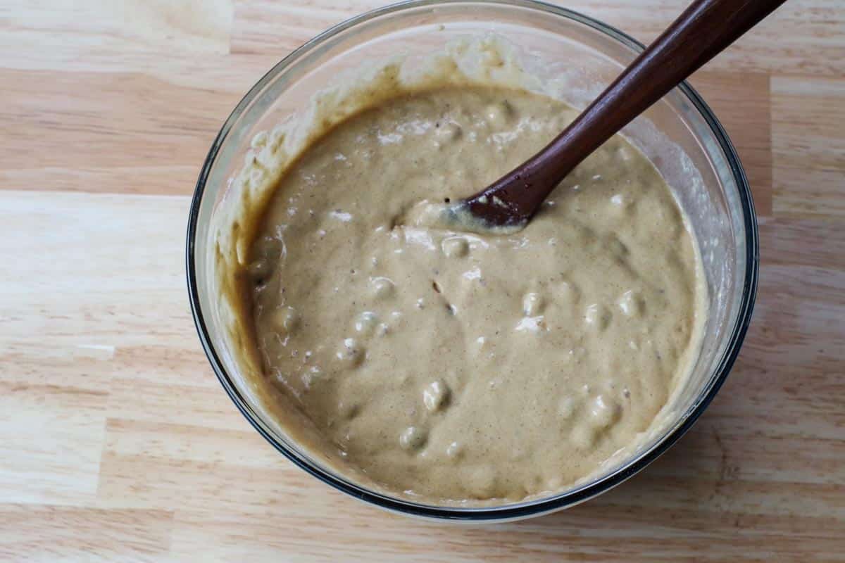 wet ingredients and dry ingredients mixed together into a batter, in glass bowl, with wooden spoon