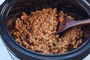 slow cooker baked beans cooked in a crockpot with a wooden spoon