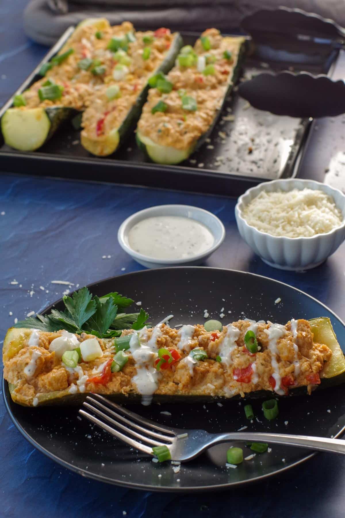 buffalo chicken zucchini boat on black plate with tray of zucchini boats in the background