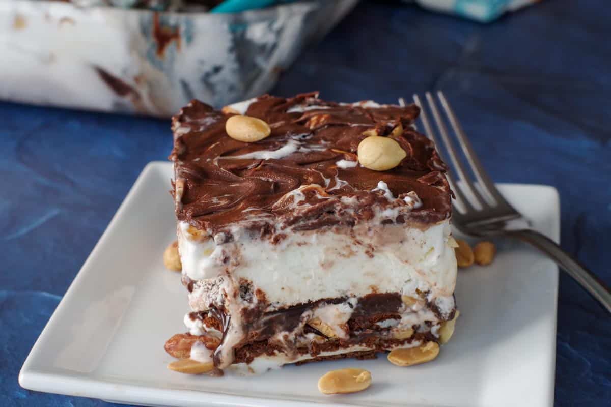 piece of buster bar ice cream cake on white plate with fork and whole glass pan in background