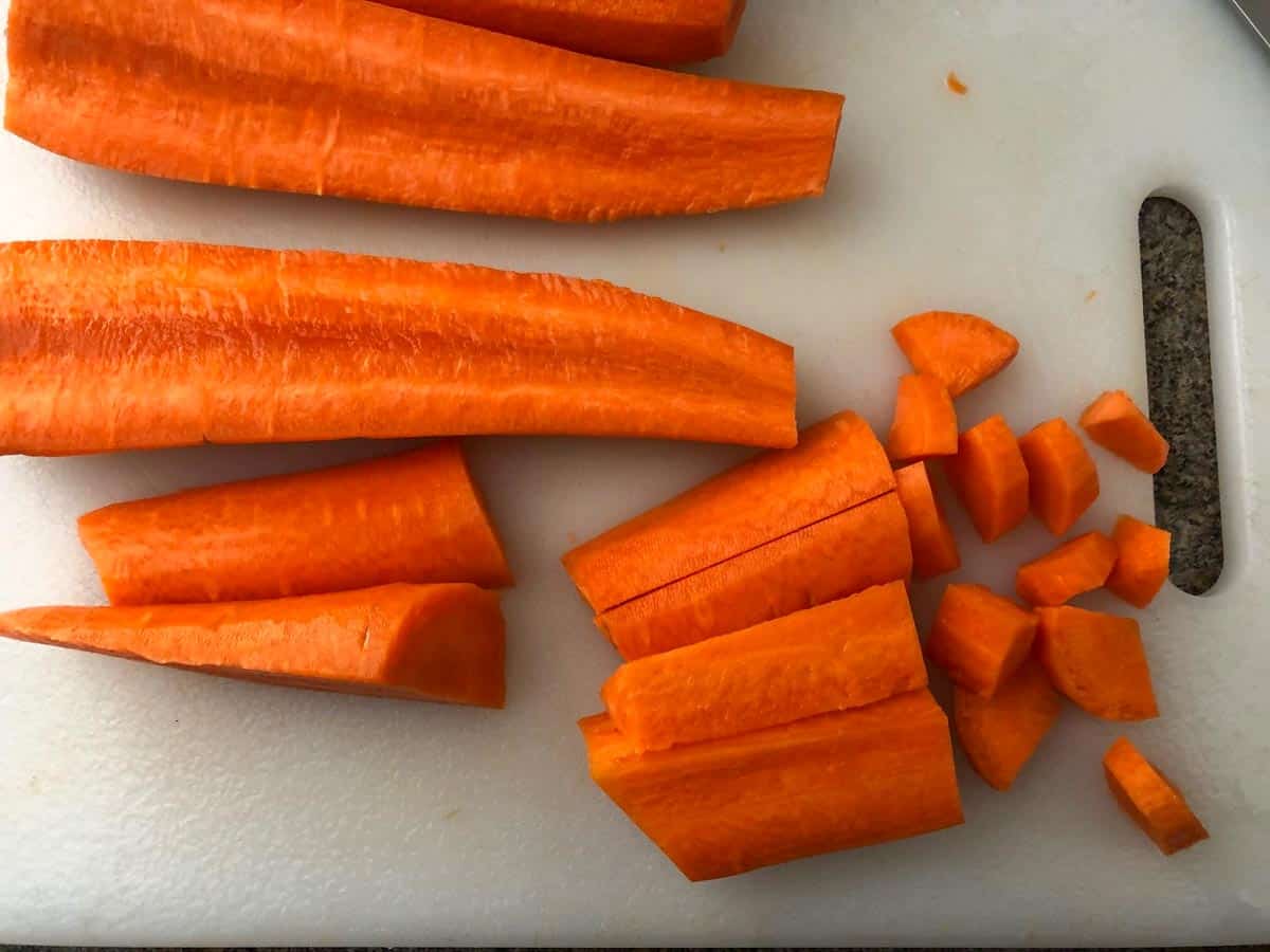 carrots being chopped into small pieces on white cutting board