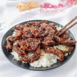 ginger beef over rice on a black plate with chopsticks