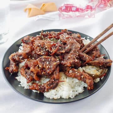 ginger beef over rice on a black plate with chopsticks