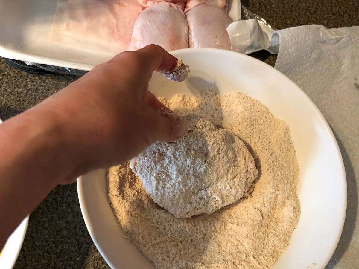 chicken being coated with breading mixture in white bowl