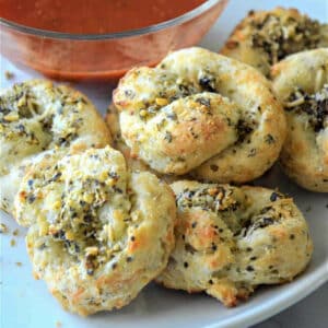 Keto garlic knots on a white plate with dipping sauce in the background