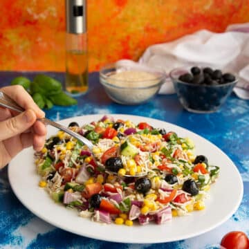 Italian rice salad on a white plate with hand holding fork in salad