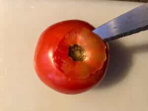 knife cutting off top of tomatoes with a cutting board