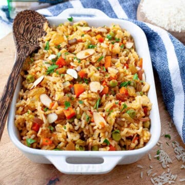 vegetarian rice pilaf in a white casserole dish on wooden surface, with large spoon in it